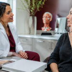 Dentist discussing lower-face aesthetic goals with an adult patient beside a facial anatomy model and professional training materials.